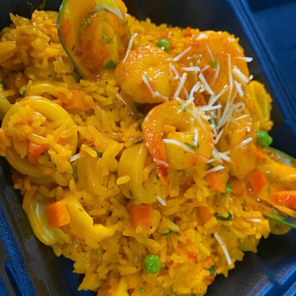 Close-up of yellow seafood paella with shrimp, calamari, peas, carrots, and shredded cheese.