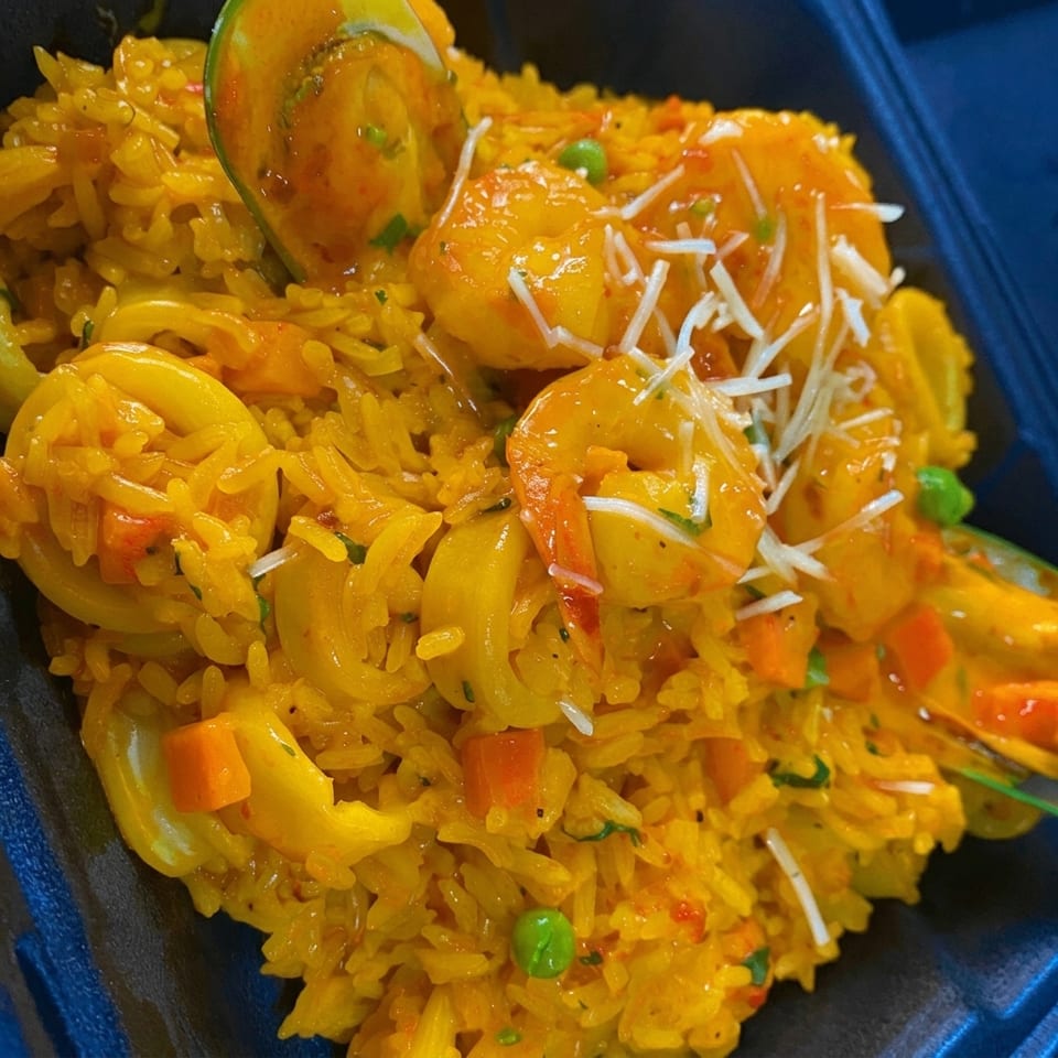 Close-up of yellow seafood paella with shrimp, calamari, peas, carrots, and shredded cheese.
